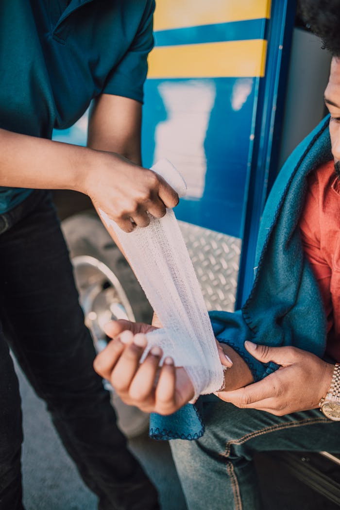 A first aid procedure with a bandage on an injured arm, outdoors near a vehicle.